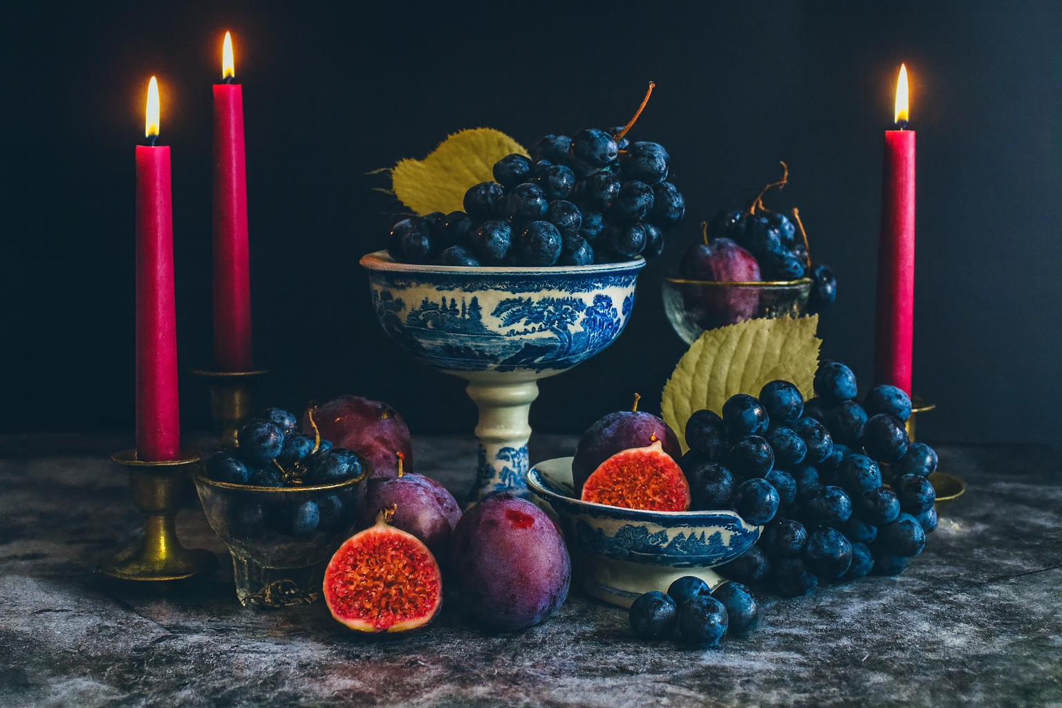 Still life arrangement with grapes, figs, and candles on a dark background