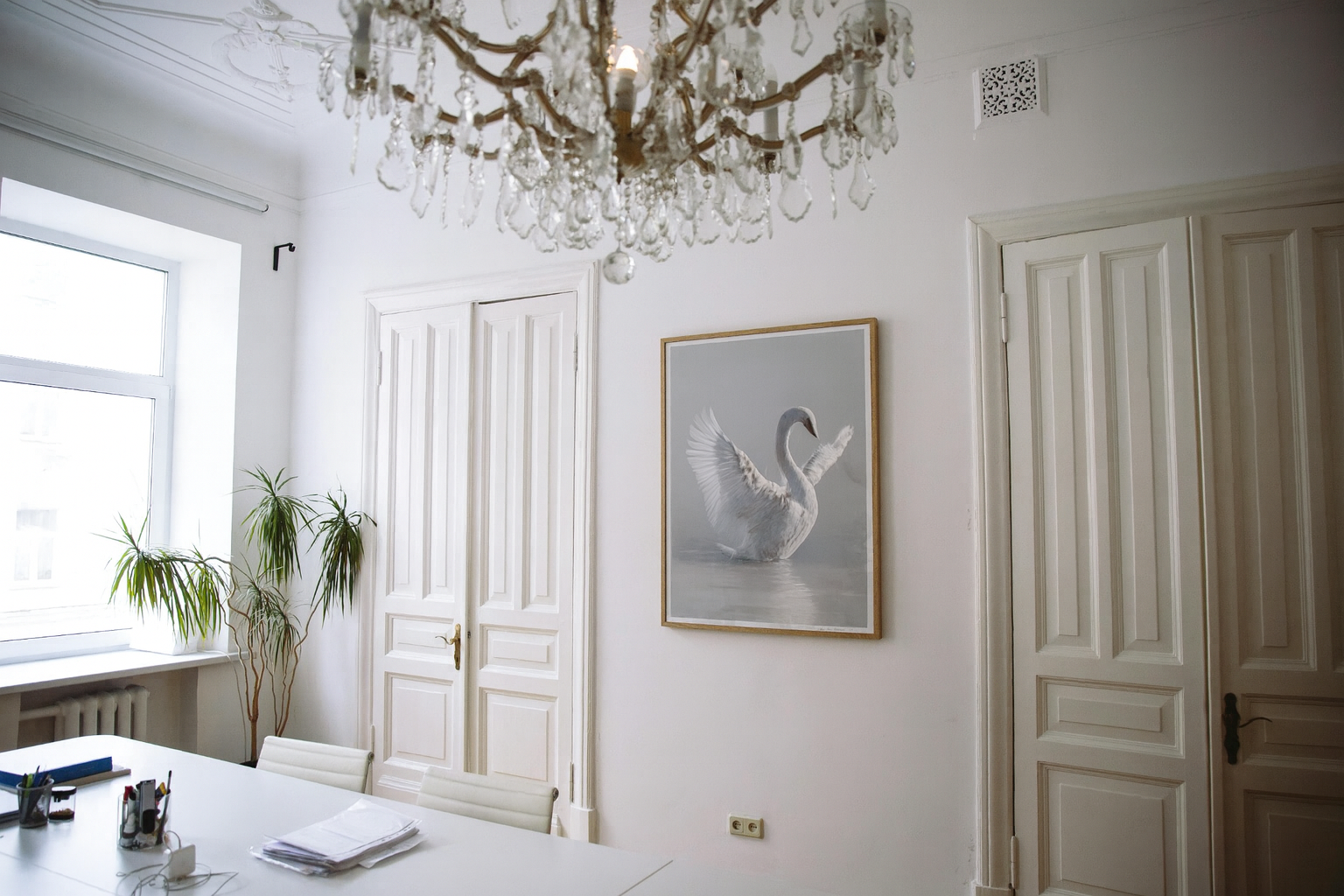 Elegant room with a chandelier, framed artwork of a swan, and white furniture.